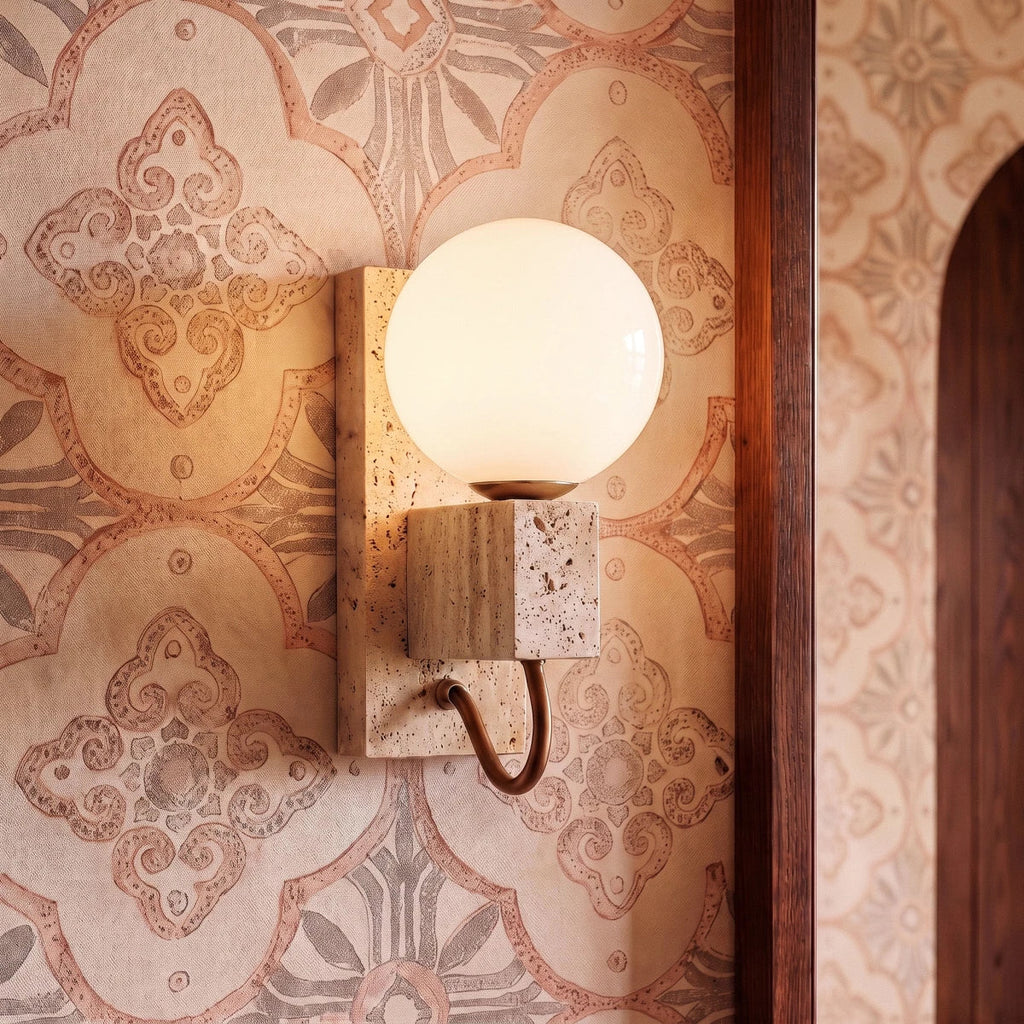 Clérachic wall lamp glowing against patterned wallpaper beside a dark wood-framed doorway to a hallway.