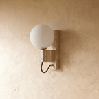 Clérachic wall lamp in travertine and brass, the opal glass globe shown glowing from another angle.