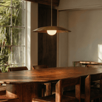 This brass Clérachic pendant light lights a live-edge dining table beside a garden-view window.