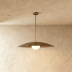 Clérachic pendant light in vintage brass with a wide saucer shade and glowing opal glass diffuser below.