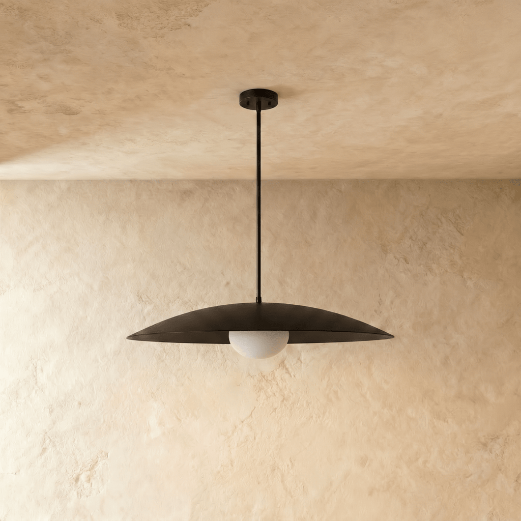This black Clérachic pendant light is shown at an angle, the opal glass diffuser glowing warmly beneath.