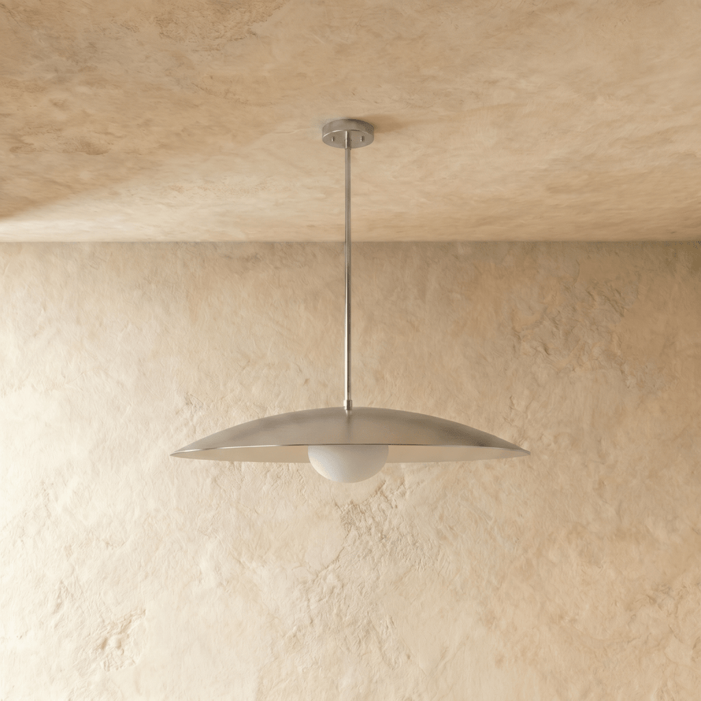 A chrome Clérachic pendant light viewed from below, the opal glass diffuser lit against a plaster wall.