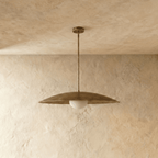 This vintage brass Clérachic pendant light is shown from a slightly different angle, its diffuser glowing warm.