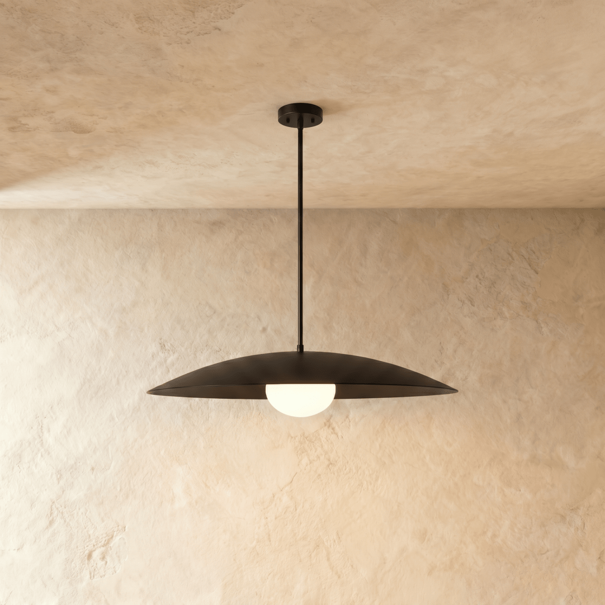 Clérachic pendant light in matte black, its wide saucer shade set above a softly glowing opal diffuser.