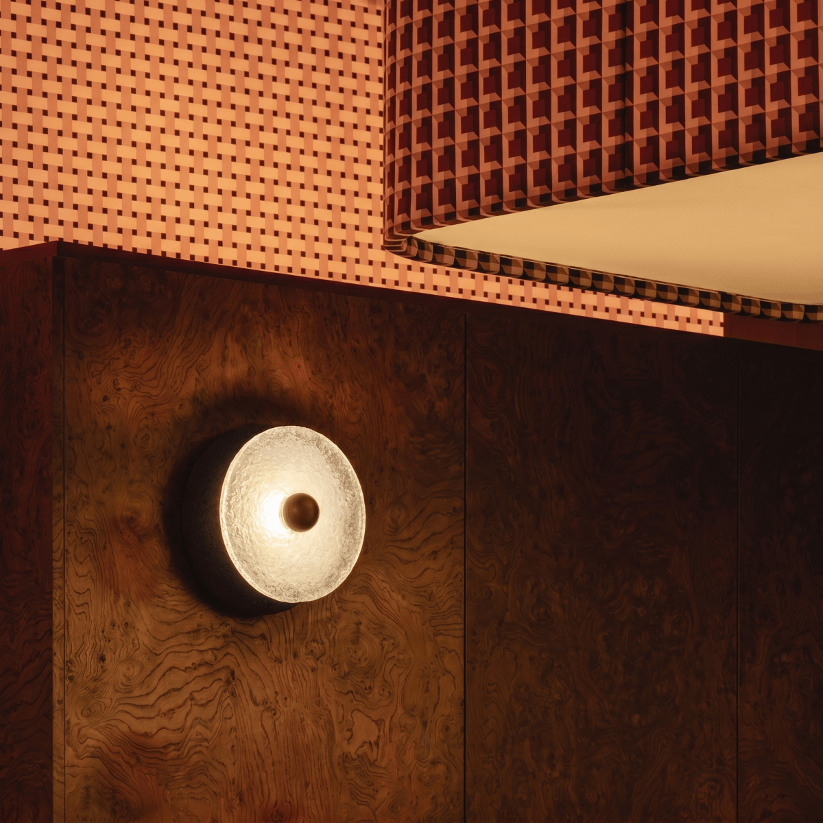 Clérachic wall lamp seen at an angle on a burl-wood panel, showing its glass front as a deep dish and the dark body standing proud of the wall.
