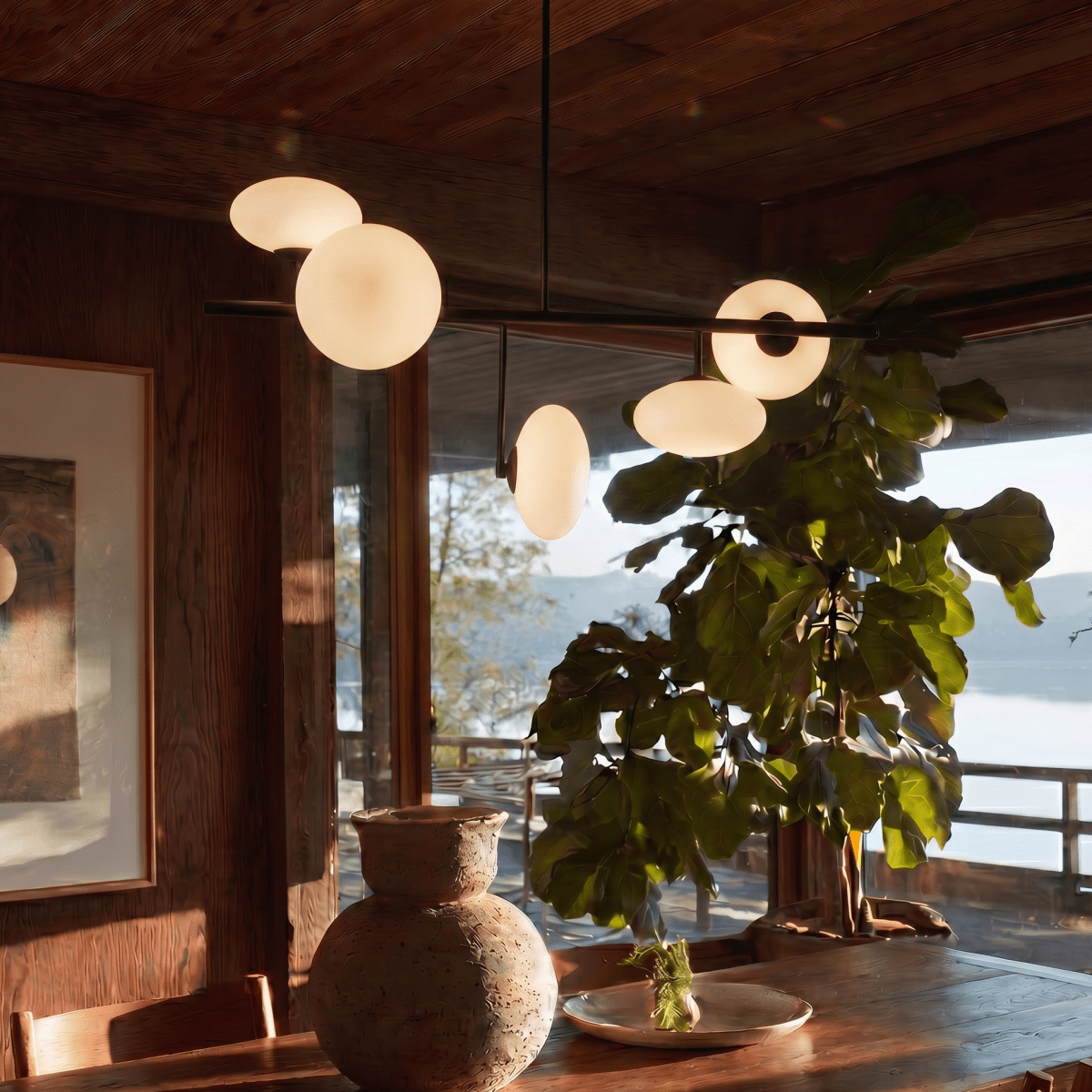 Clérachic sculptural chandelier hanging above a wood dining table set with a ceramic vase, a plate and a leafy fig plant.