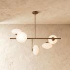 Clérachic sculptural chandelier in a vintage brass finish, its lit sphere overlapping the flattened lens shade at one end of the bar.