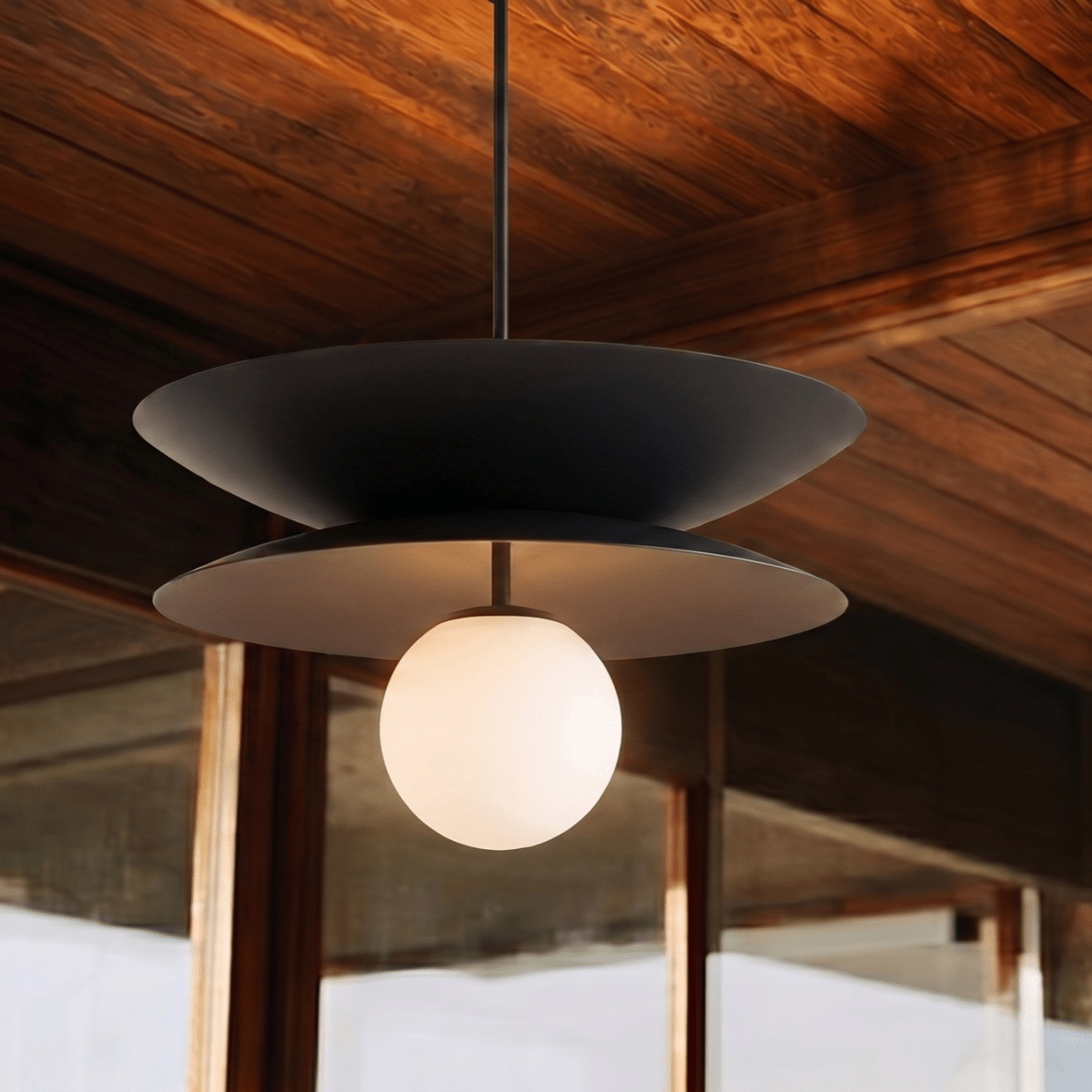 Clérachic double-disc pendant light in matte black, glowing beneath a sunlit tongue-and-groove plank ceiling.