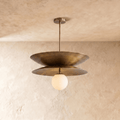 Clérachic double-disc pendant light in vintage brass, hanging from a plain plaster ceiling with its white glass globe unlit.