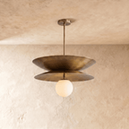 Clérachic double-disc pendant light in vintage brass, hanging from a plain plaster ceiling with its white glass globe unlit.