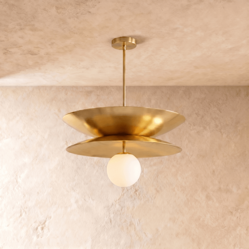 Clérachic layered-disc pendant light in polished brass, its two saucer discs warm gold against a bare plaster wall.