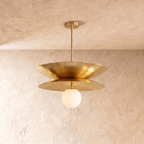 Clérachic layered-disc pendant light in polished brass, its two saucer discs warm gold against a bare plaster wall.