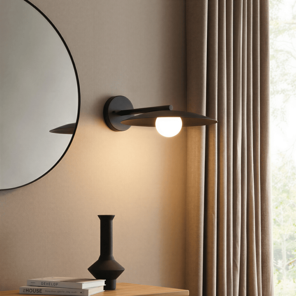 Clérachic wall lamp in black beside a round mirror, its shade rim passing clean through the wall plate above a console table.