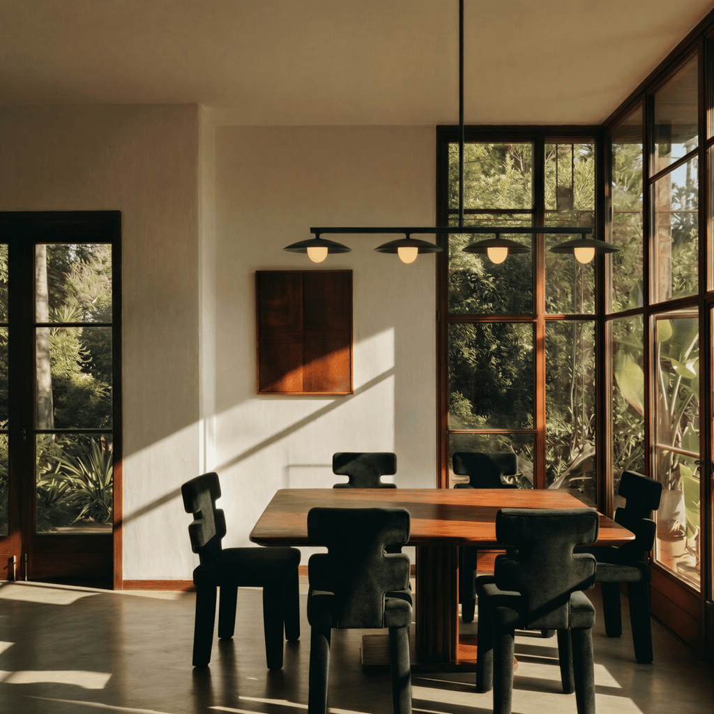 Clérachic black pendant light centred over a dining table ringed with sculptural dark chairs, tall dark-framed windows opening onto greenery behind.