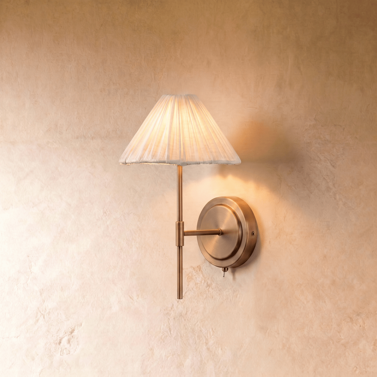 This Clérachic wall light pairs a pleated ivory fabric shade with a slender brass stem and pull-chain switch.
