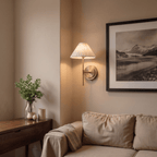 A Clérachic wall light glows warmly in a room corner beside a framed black-and-white landscape print.