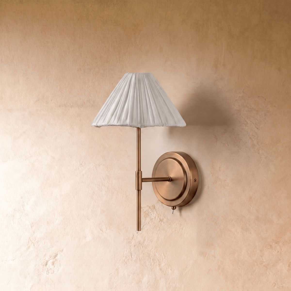 A Clérachic wall light's pleated cone shade sits atop a brass stem mounted on a round wall plate.