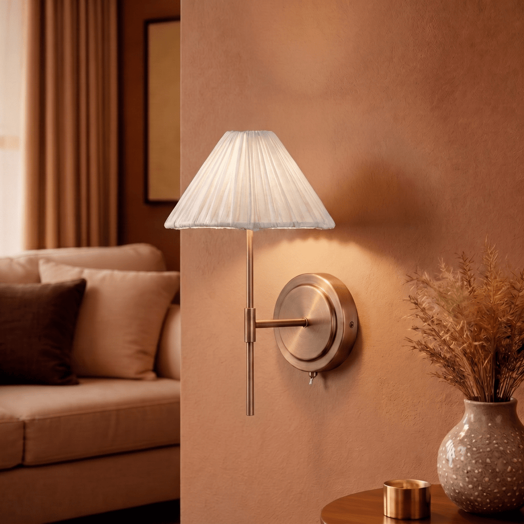This Clérachic wall light glows warmly beside a sofa, its pleated shade set against a terracotta wall.