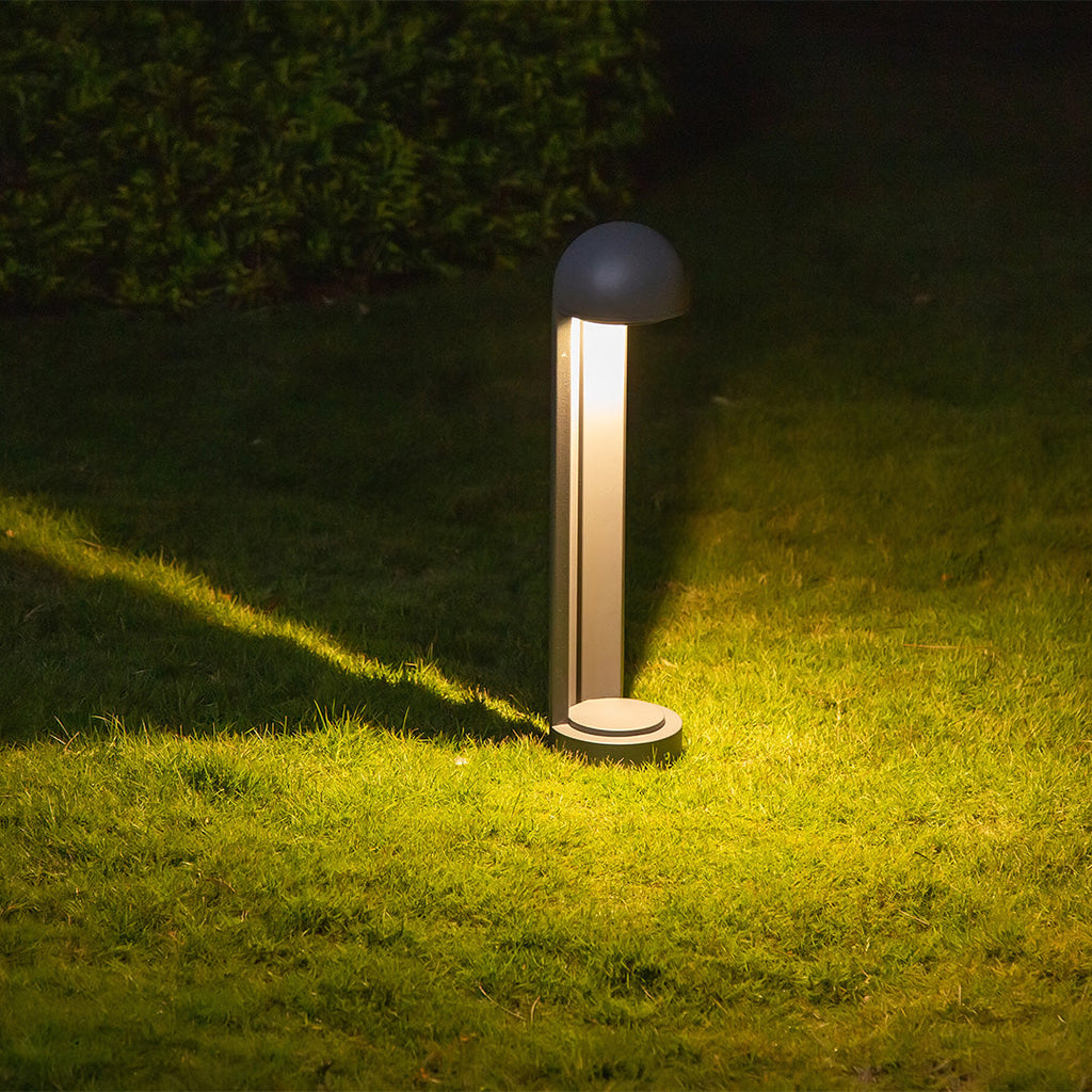 A single bollard lit at night on a lawn, its glow pooling across the grass.