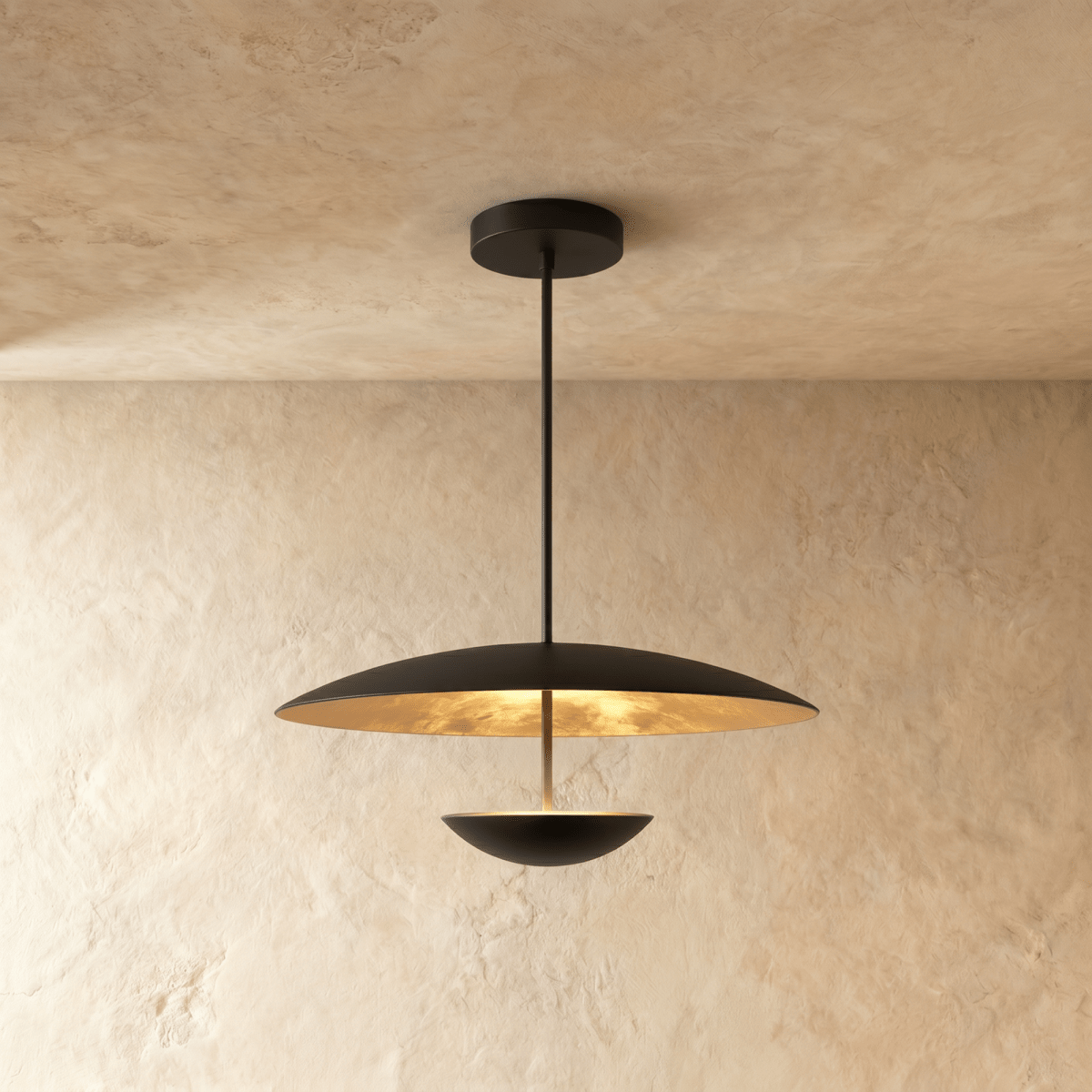 Clérachic pendant light in matte black, its brass-toned inner face lit above a black bowl edged with a thin line of light.