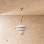 A Clérachic pendant light's tiered opal glass shade catches warm light beneath a brass ceiling mount.