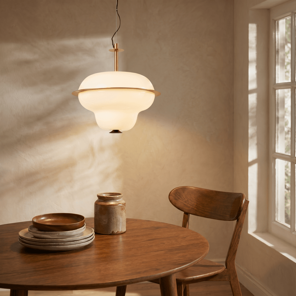 A Clérachic pendant light glows above a round wooden dining table set with rustic plates and a jug.